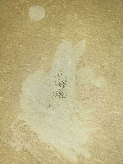 Sliten plastmatta på garderobsgolv med synligt nätmaterial, blekt område och fläckar, eventuellt linoleum; problem vid skurning.