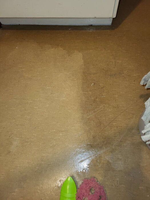 Slitet golv i garderob med rengjorda och smutsiga ytor samt rengöringsverktyg synliga längst ner i bild.