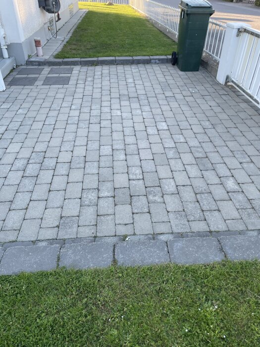 Gräsmatta med övergång till stenlagt område, kantsten skiljer ytorna. En soptunna syns till höger. Diskussion om installation av Automower.