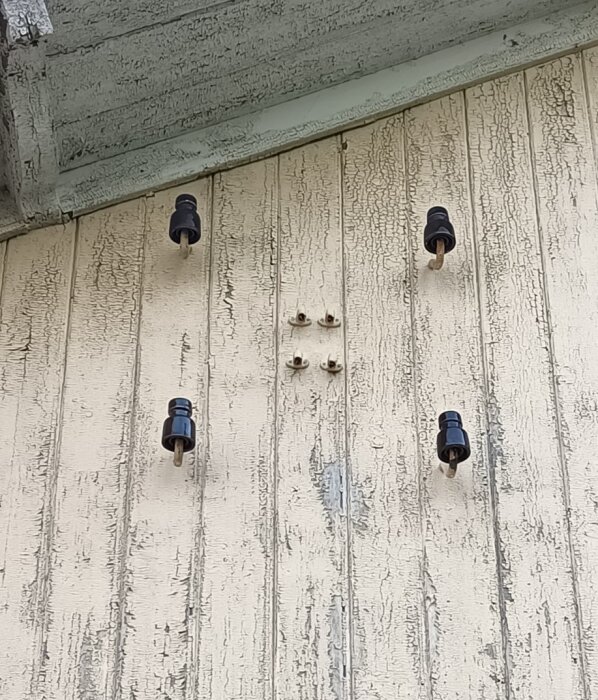 Vägg med flera svarta elisolatorer monterade på en yta med sprucken färg.