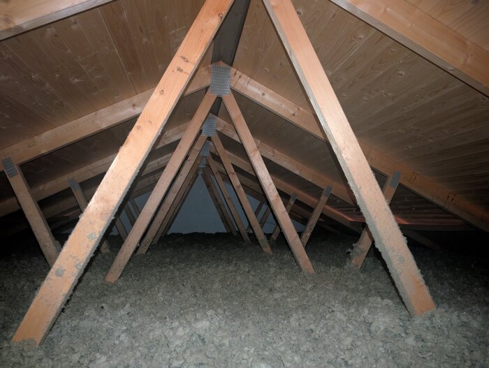 Takstolar ovanför ett garage sedda från vinden, med isolering på golvet och träpaneler i taket.