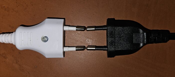Vit och svart elkontakt som är på väg att kopplas ihop på ett brunt underlag.
