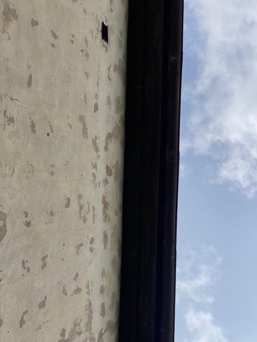 Reveterad husfasad med ojämn puts och synliga lagningar under en blå himmel.