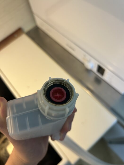 Inloppsslangens ände för en diskmaskin med en röd insats, hållen ovanför en köksbänk.