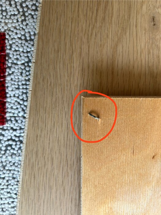 Parkettgolv med en krokig spik markerad med röd cirkel, del av renoveringsarbete.