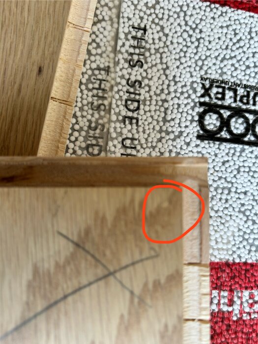 Parkettgolv med markerad träbräda och underliggande isolering med texten "THIS SIDE UP" sedd ovanifrån.