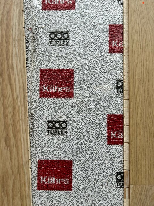 Underlag under parkettgolv med märkena "Kährs" och "Tuplex", samt parkettbrädor synliga på sidan.