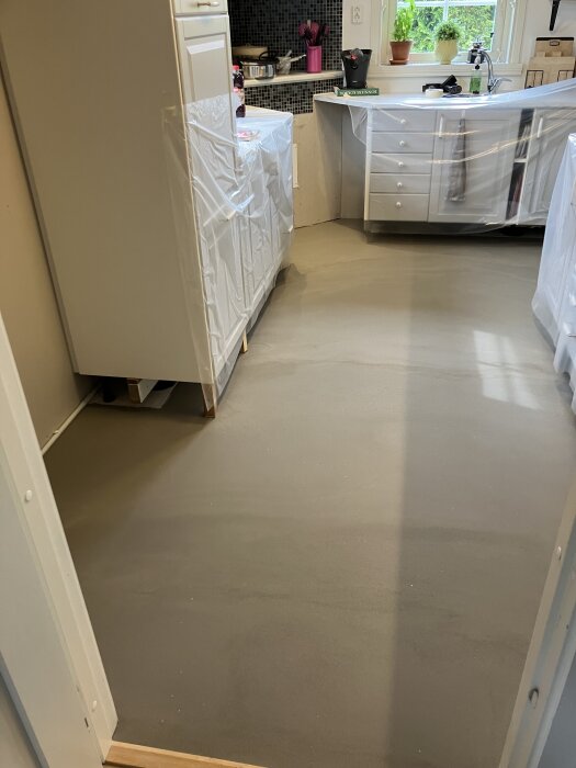 Nyligen flytspacklat köksgolv med plasttäckta skåp och utrustning, redo för golvläggning.