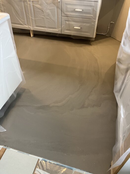 Nylagt flytspackel på golv i rum med täckta köksluckor, redo för golvläggning.