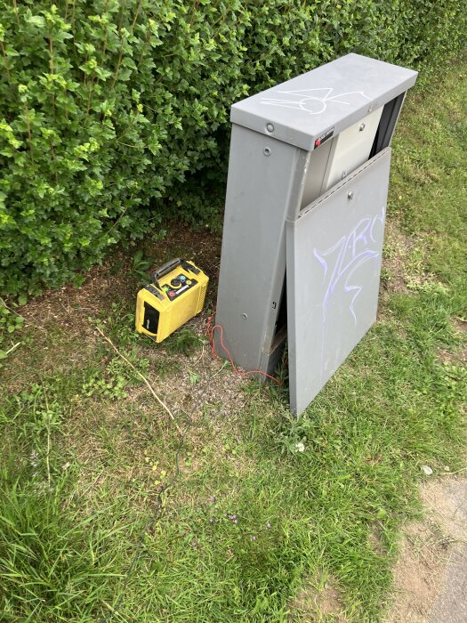Öppnat elskåp vid häck med ansluten gul mätlåda och jordkontakt.