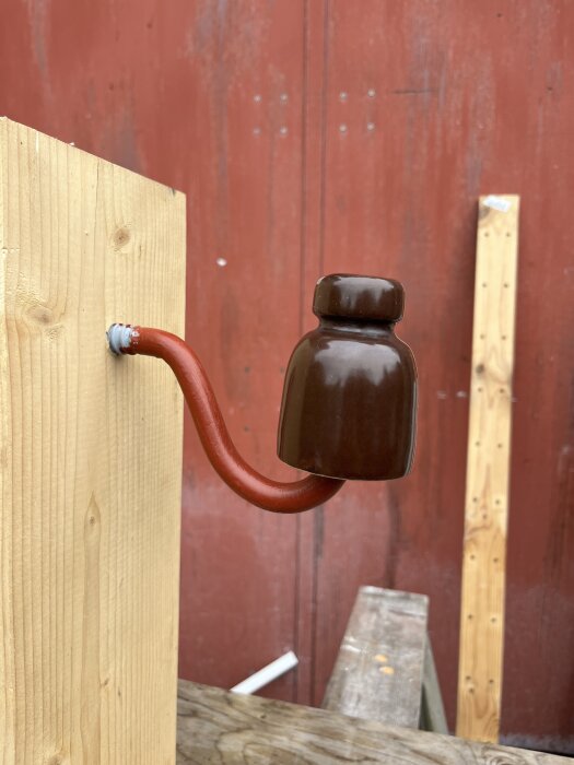 Rengjord och påmålad brun insulator fäst på en träbräda framför en röd vägg, redo för montering.