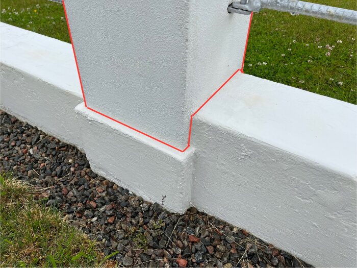 Betongmur med röd markeringslinje som visar delarna av puts och tegel som ej ska slipas. Muren omges av gräs och grus.