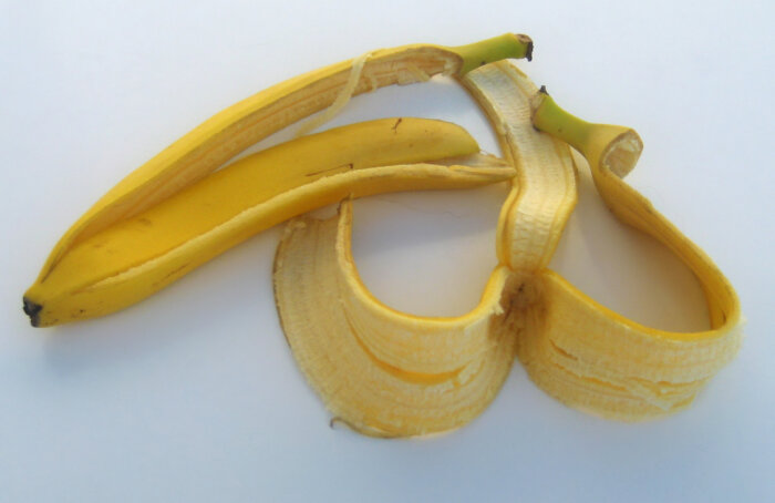 Ett halvt avskalat bananskal ligger på en vit yta, bananskalet är krökt och guldfärgat.