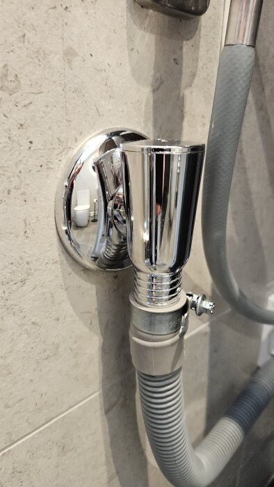 Avloppsanslutning med kromdetaljer på en vägg, visar stängd koppling av en grå slang, kan tyda på ventilationsproblem för tvättmaskinen.