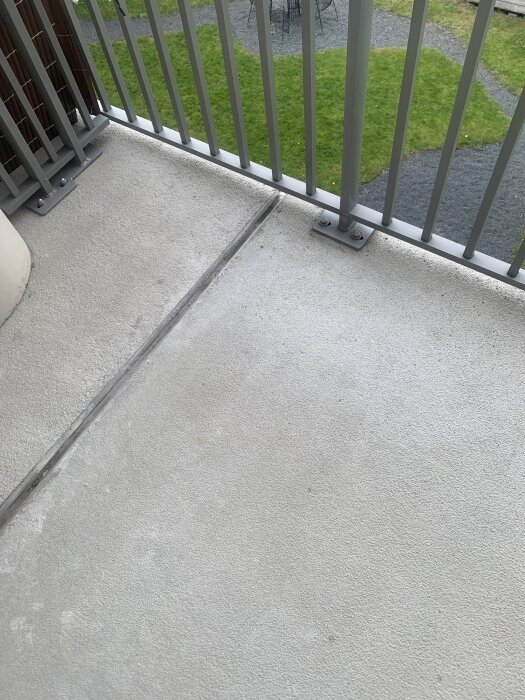 Balkonggolv med obestämda smutsfläckar intill ett metallräcke och utsikt över en gräsmatta.