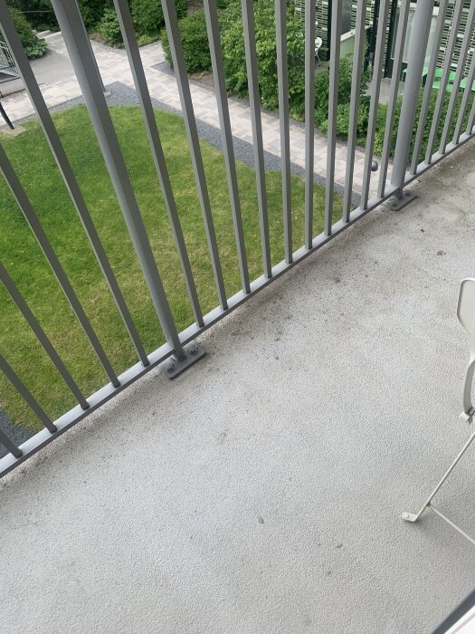 Balkonggolv med oidentifierade smutsfläckar, metallräcke och grön utsikt i bakgrunden.