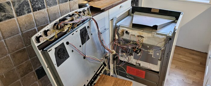 Öppen köksspis med blottade ledningar och trådar inuti, stående i ett kök.
