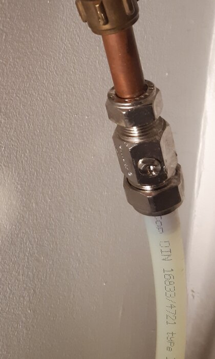 Närbild på en 12/15 mm kulventil ansluten till koppar- och plastledning, mot en vit vägg.