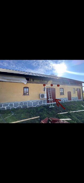 Gult hus med svart tak, stege lutad mot fasaden. Röd pil pekar på igenmurad öppning där en fönsterdörr planeras att sättas in.