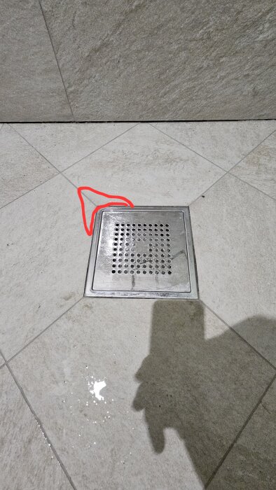 Duschklinkergolv med golvbrunnssil där en liten vattenansamling visas vid hörnet markerat med röd linje.