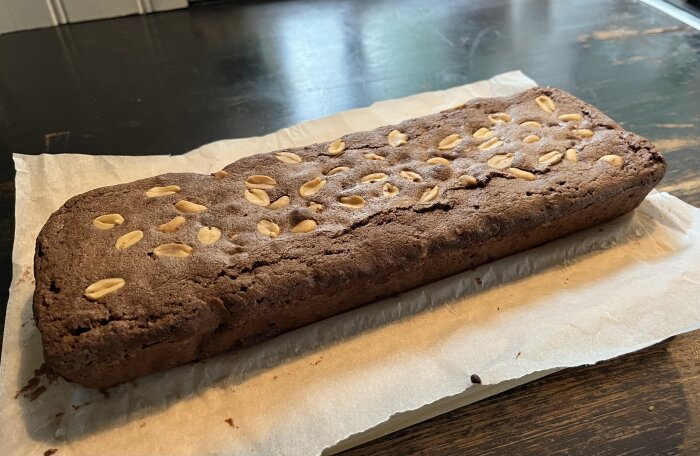 Hemmagjord kaka med nötter på toppen, placerad på bakplåtspapper på ett bord.