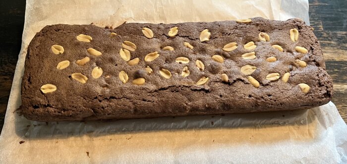 Hemmagjord chokladkaka med jordnötter ovanpå, lagd på bakplåtspapper.