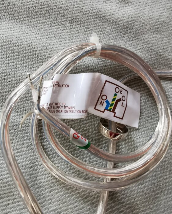 Genomskinlig elkabel med etikett och blottade trådar, placerad på en texturerad yta.