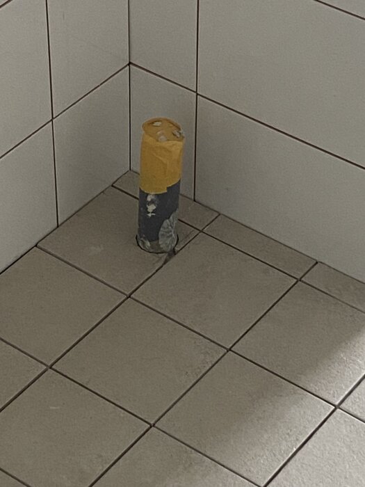 Ett kaklat badrumsgolv med ett avloppsrör där en kakelplatta har en spricka runt röret.