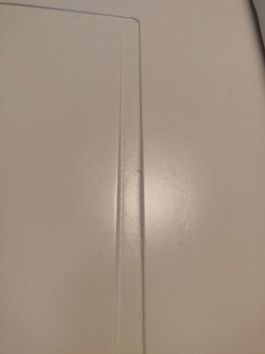 En närbild av en vit dörr med en inskärning eller spår längs kanten, ytan ser slät och målade ut.