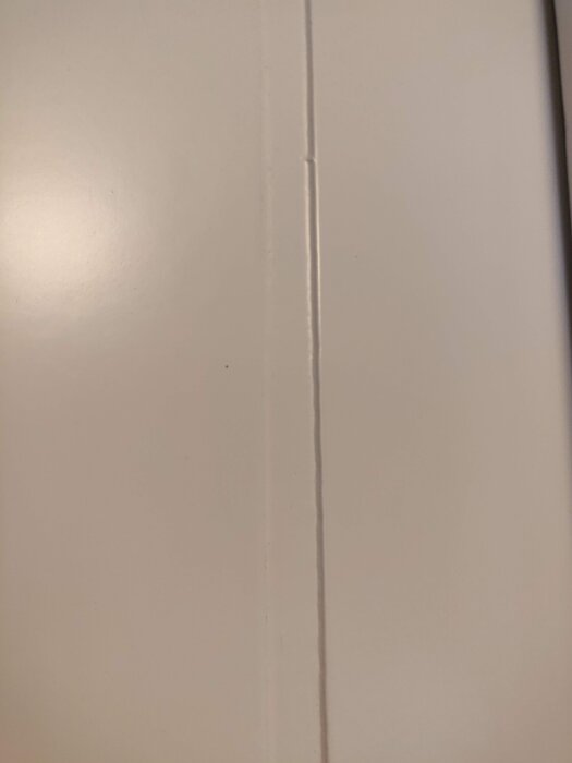 Närbild av en del av en dörr med en vertikal skåra, visar ytans struktur och skårans profil.