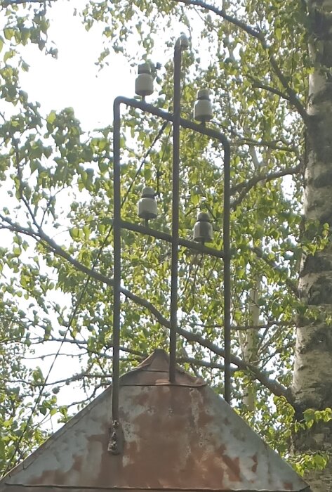 Rostigt pumphus med metallstänger och isolatorer, omgiven av trädgrenar och lövverk i bakgrunden.