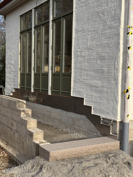 Stentrappa vid utbyggnad, med lecablock på sidan och betongplattor ovanpå. Husets fasad med stora fönster syns i bakgrunden.