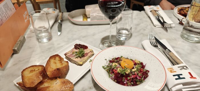 Råbiff med äggula och grönsaker samt en skiva anklever med gelé på ett marmorbord, serverat med vin.