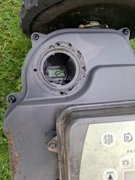 Närbild av en Husqvarna robotgräsklippares öppnade chassi med en synlig elektronikkrets inuti, omgiven av smuts och fukt.