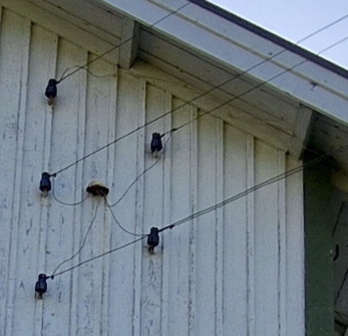 Ledningar som fästs på en husvägg och går in i huset via isolatorer, separerade från andra elkablar.