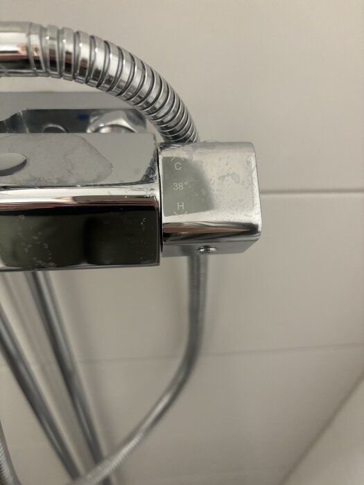 Kromad duschblandare med vred vid 38 grader, visar temperaturinställningar. Blankt och modernt utseende med vattenfläckar.