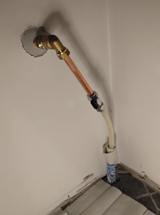Kopparrör kopplat till pex-slang genom golv, papper utlagt för att upptäcka eventuella läckor.