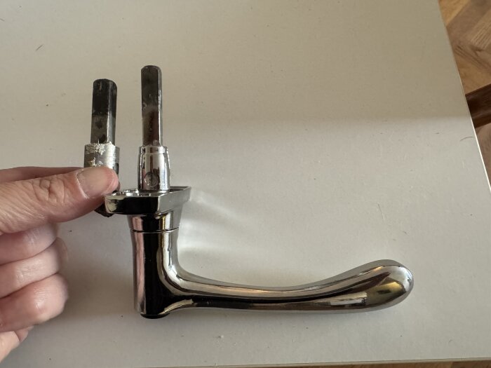 Fönsterhandtag EFO-61 med längre stav, hålls vid ett äldre, kortare handtag, på ett bord.