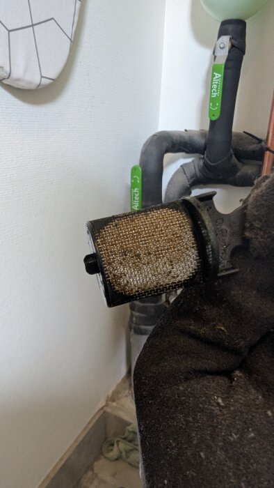 Filter med grus och smuts monterat på rörledning, procentuell genomströmning uppskattad till 60%.