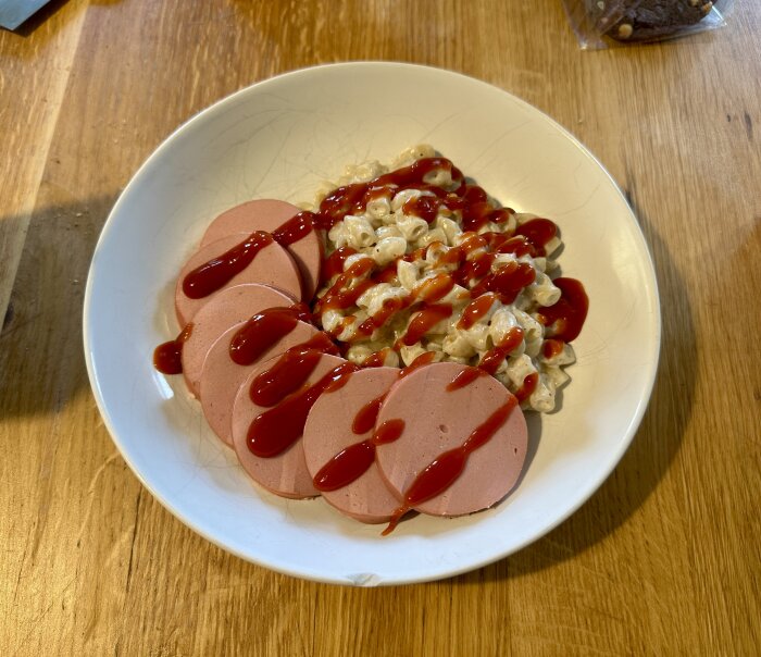 Tallrik med stuvade makaroner och Jokkmokkskorv skivor, toppad med ketchup.