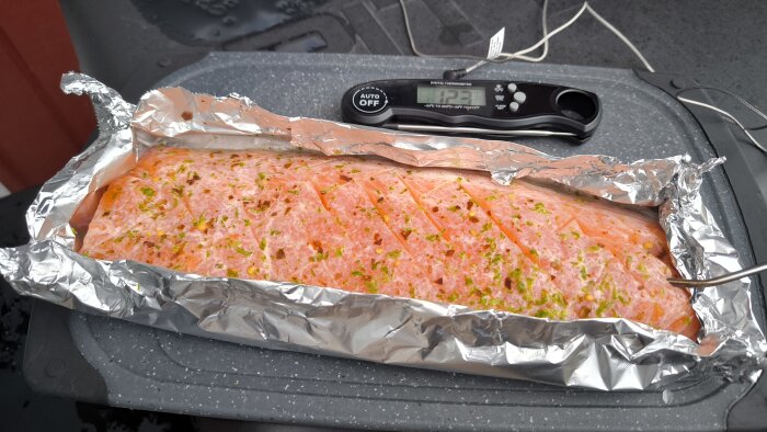 Limerökt lax med chili på en grill, inslagen i folie, med en digital termometer bredvid.