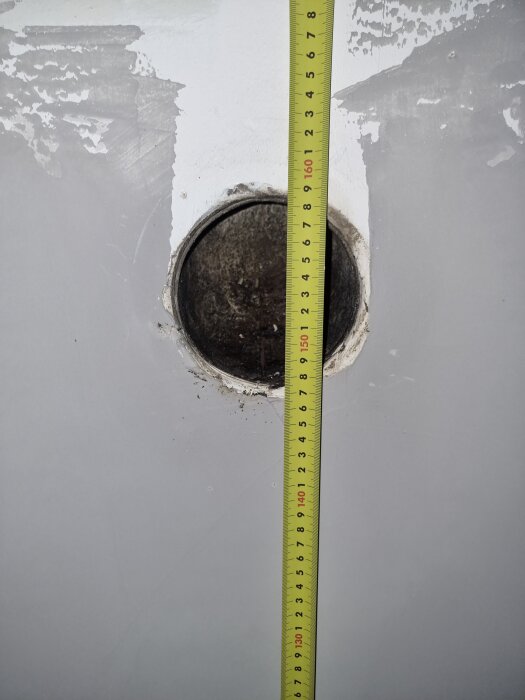 Gipsskiva med ett runt hål i mitten, ett avsågat rör inuti; gul mätstock visar 0 till 160 cm mot hålets högra sida.