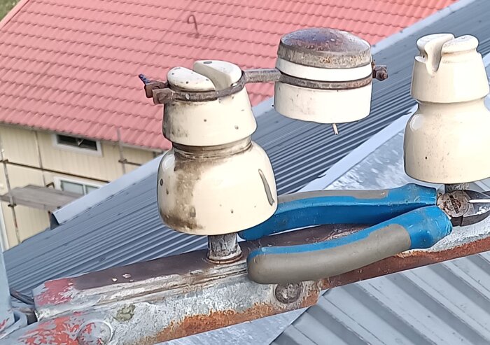 Tak med isolatorer och avbitartång nära en nock, några trådar syns vid isolatorbotten. Bakom syns ett hustak med röda takpannor.