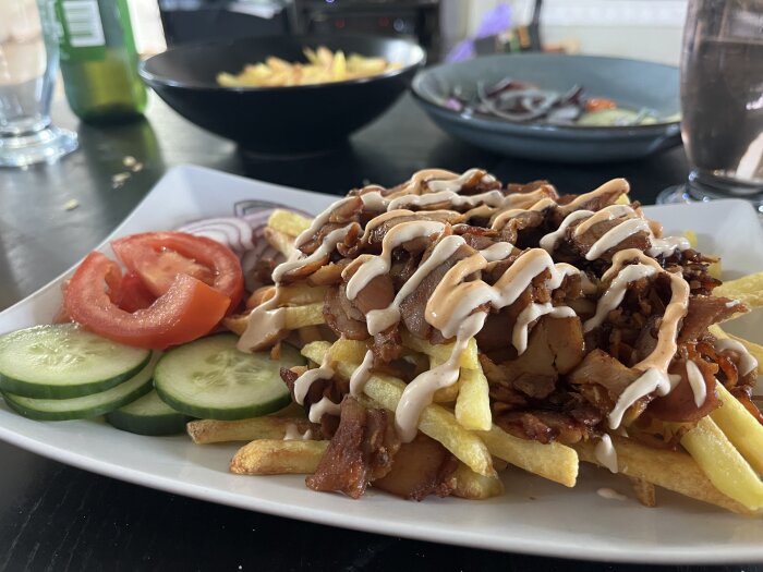 Kycklingkebab med pommes och sås på en tallrik, serverad med skivade tomater, gurkor och rödlök.