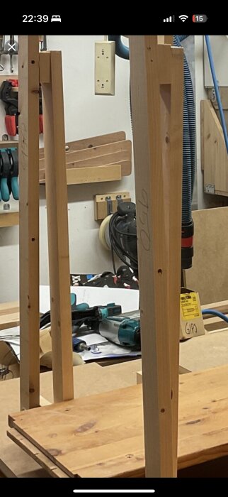 Verkstad med slipmaskin och trävirke, omgiven av verktyg och träbitar, med fokus på pågående byggprojekt.