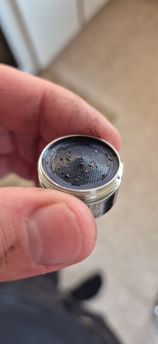 Vattenfilter från kran med grus- eller rostpartiklar efter spolning, hålls i handen.