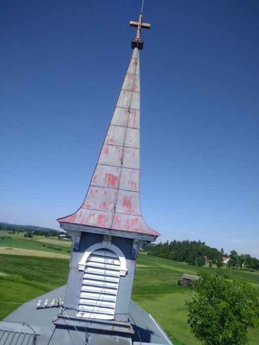 Tornet på en kyrka med åskfångare, telekablar och påhängsisolator. I bakgrunden syns gröna fält och träd.