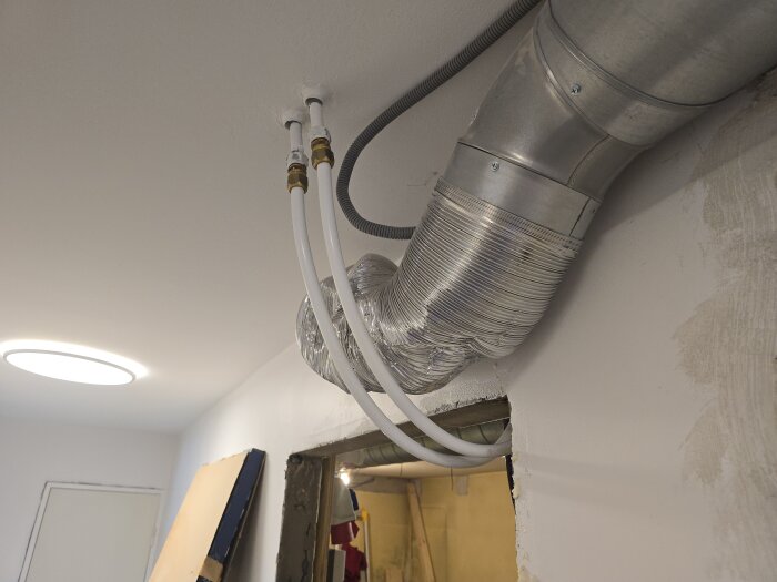 Rör och ventilation i taket, del av renovering i husets förråd. Vattenrör och en ventilationskanal syns tydligt vid en öppning i väggen.