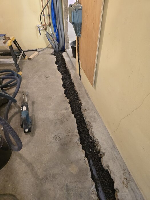 En betongränna fylld med makadam i ett förråd, omgiven av rör och verktyg på golvet, förberedd för betonggjutning.
