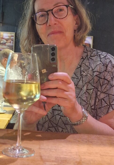 En person tar en selfie med ett glas vitt vin på ett bord, troligen på Barcelonas flygplats.